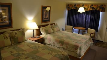 A hotel room with two beds, a desk, a chair, and a small table.