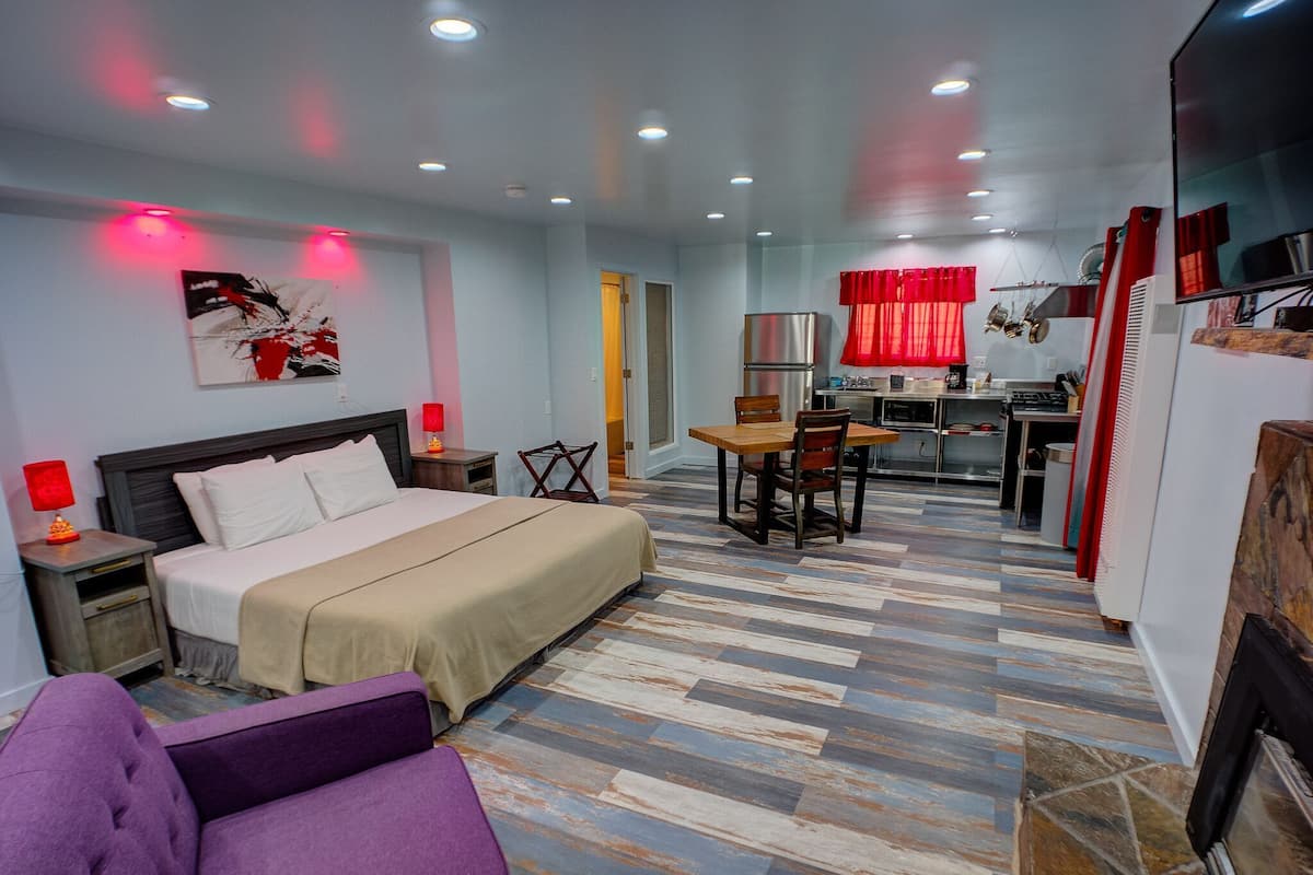 Una habitación de hotel con cama, una mesa de comedor con sillas, kitchenette, televisor y sofá púrpura.
