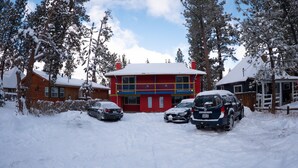 Un edificio de dos plantas con fachada roja y azul, rodeado de árboles cubiertos de nieve y coches aparcados.