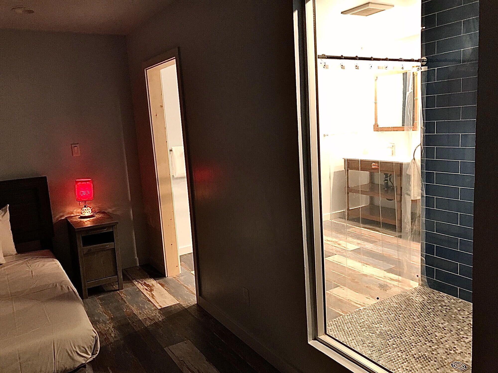 Camera d'albergo con un letto, un comodino con una lampada, una porta che dà su un balcone e vista all'esterno.