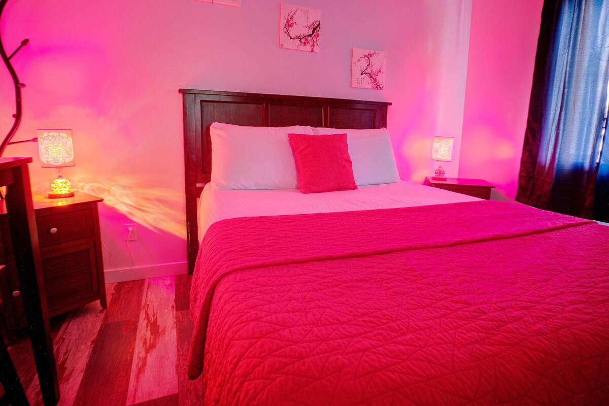 Una habitación con cama, mesita de noche, lámpara y decoración en la pared.
