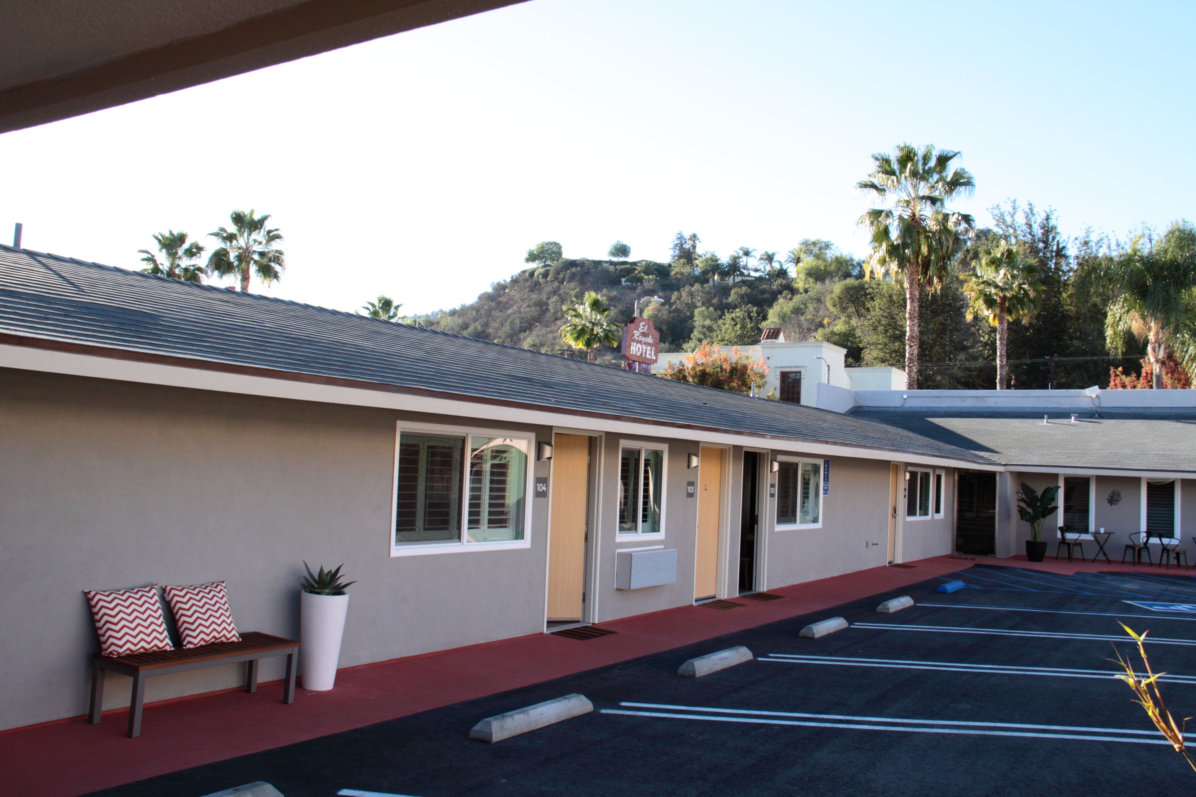 A motel with a red carpeted walkway, a bench with patterned cushions, and a parking lot with marked spaces.
