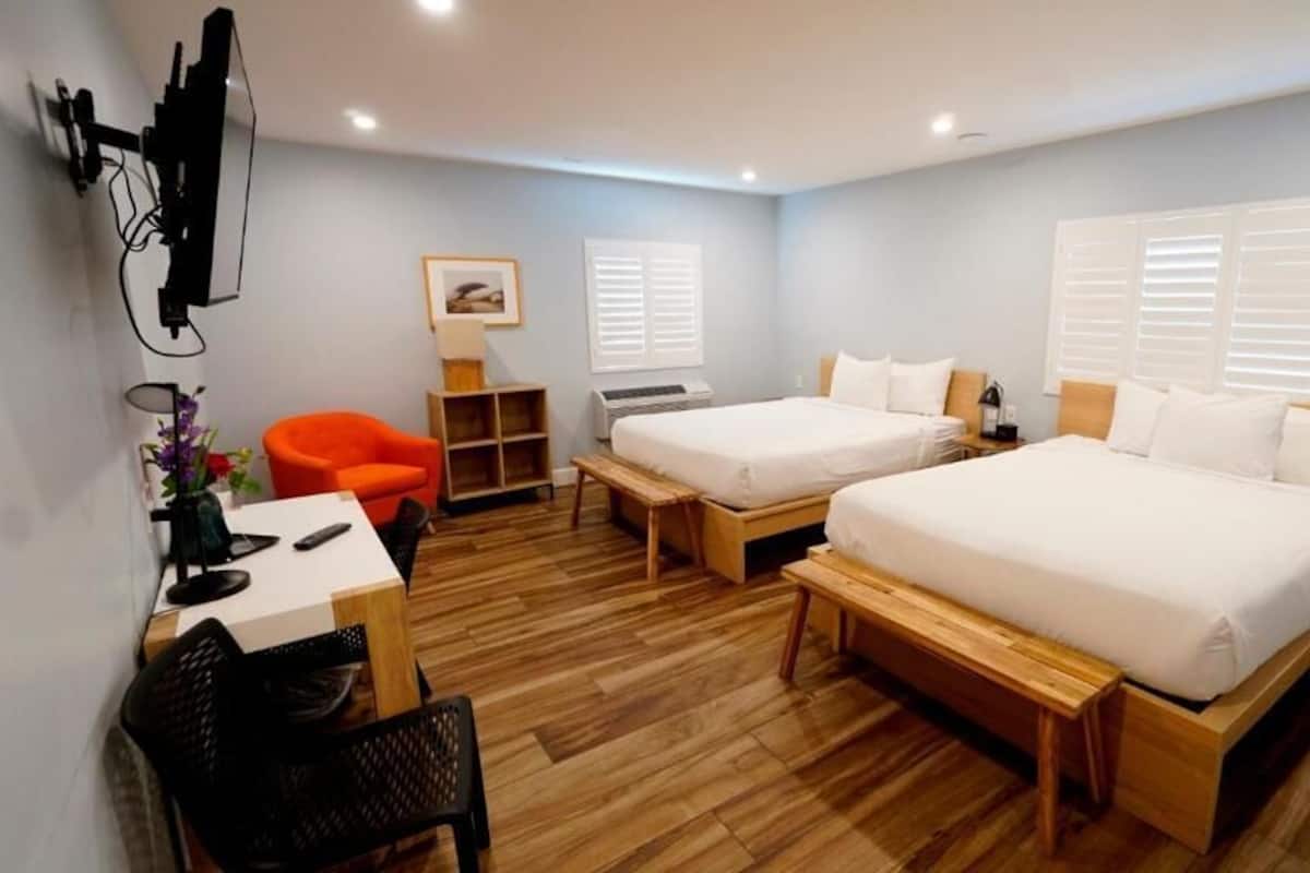 Habitación de hotel con dos camas, un escritorio, una silla, un televisor y una ventana con contraventanas.