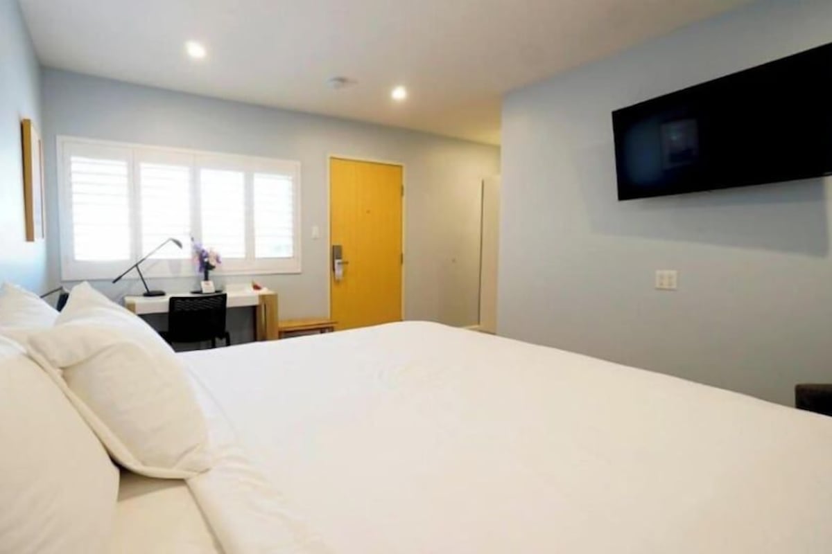 Une chambre d’hôtel avec un lit, un bureau, une chaise, une télévision et une fenêtre.