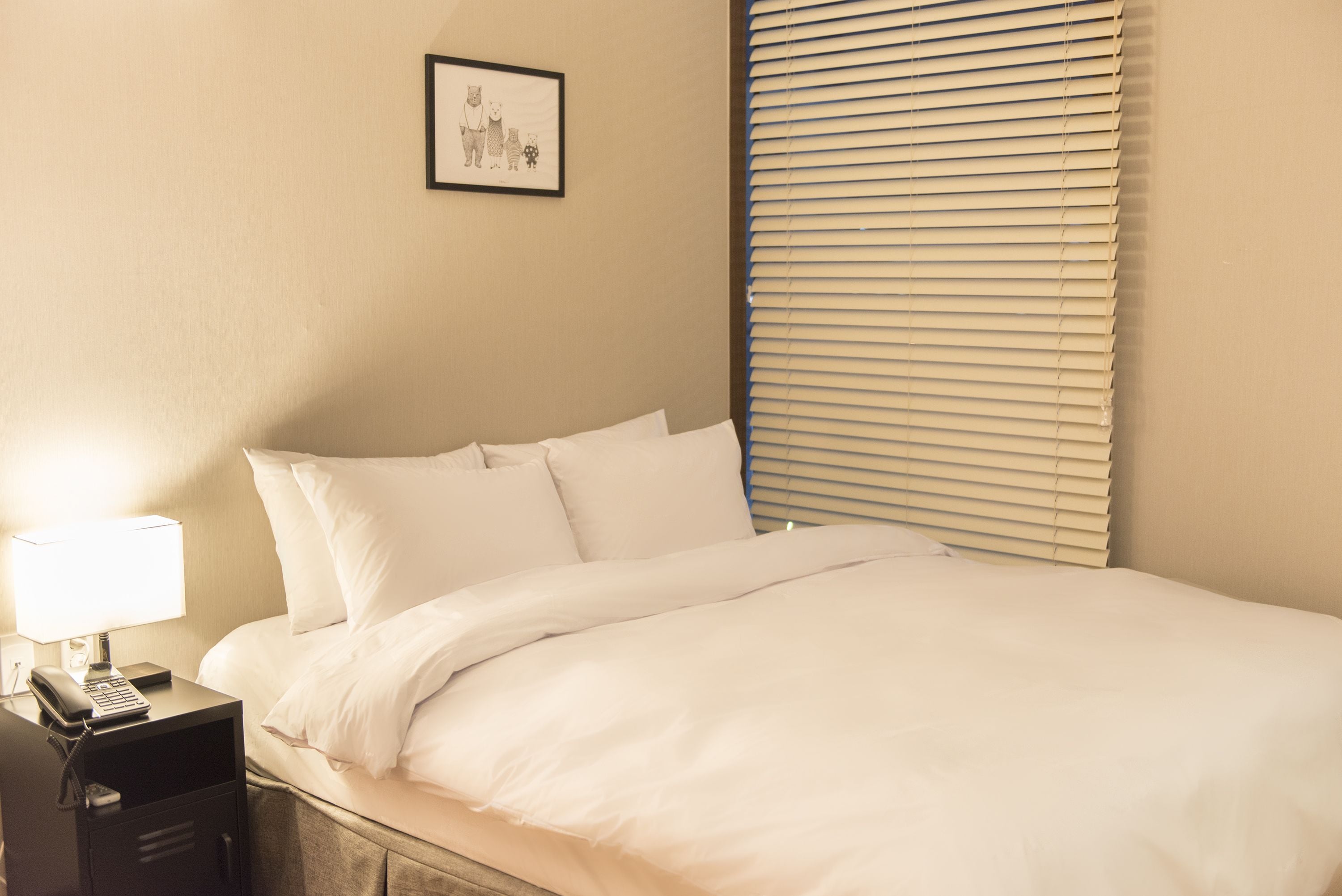 A neatly made bed with white linens, a bedside lamp, and a framed picture on the wall.