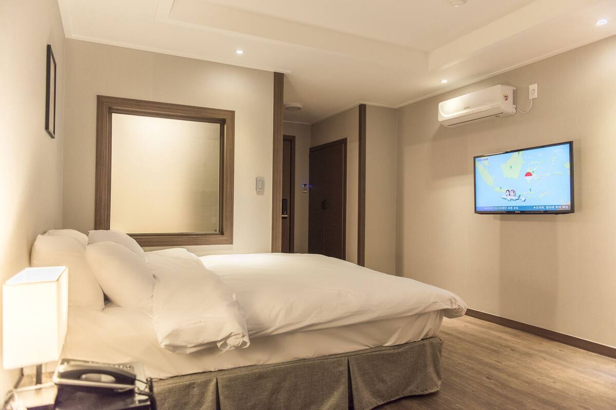 A hotel room with a large bed, a television mounted on the wall, and a ceiling-mounted air conditioning unit.