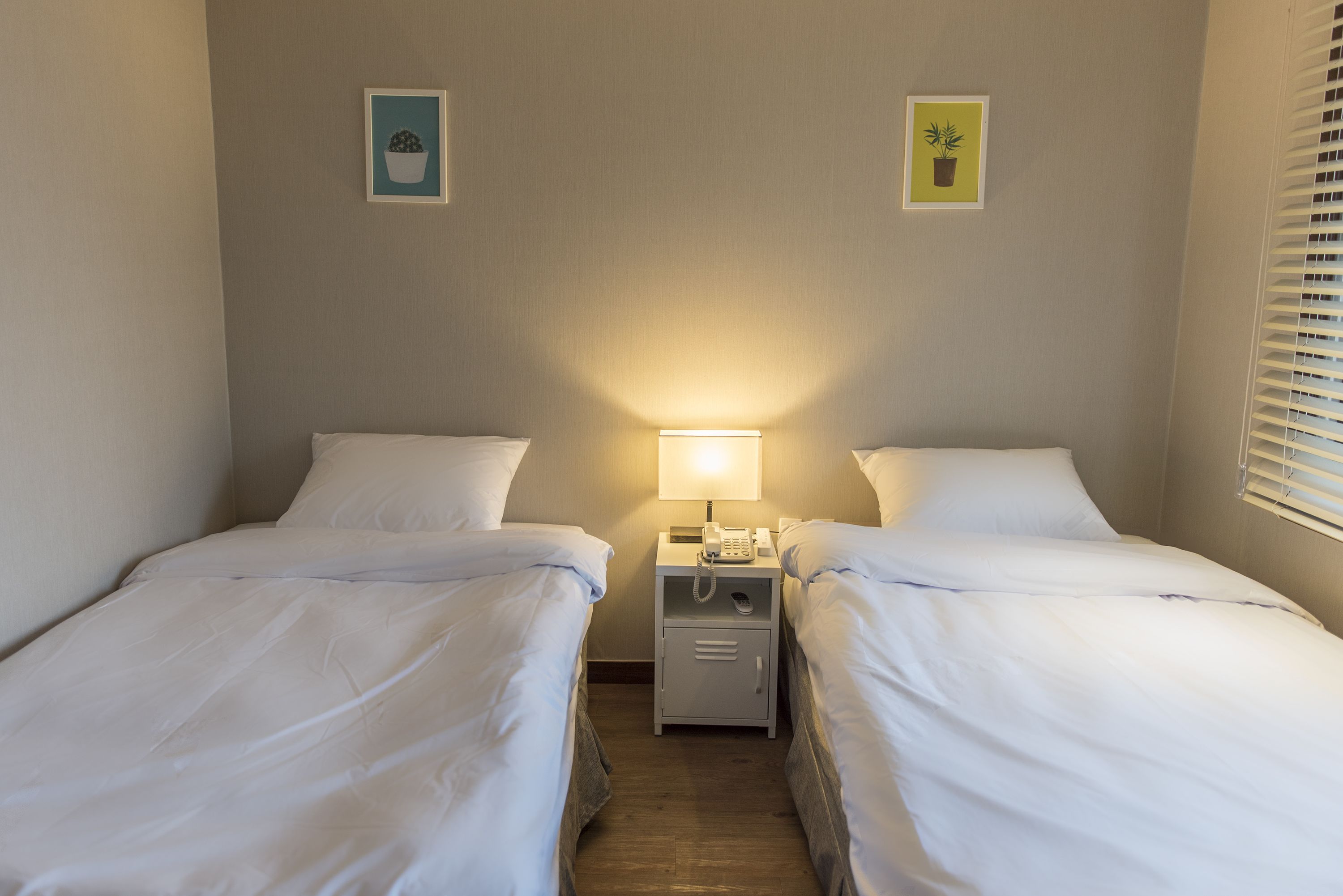 Una habitación de hotel con dos camas individuales, una mesita de noche con lámpara y un pequeño armario.
