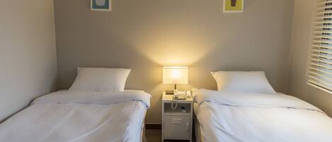 Una habitación de hotel con dos camas individuales, una mesita de noche con lámpara y un pequeño armario.