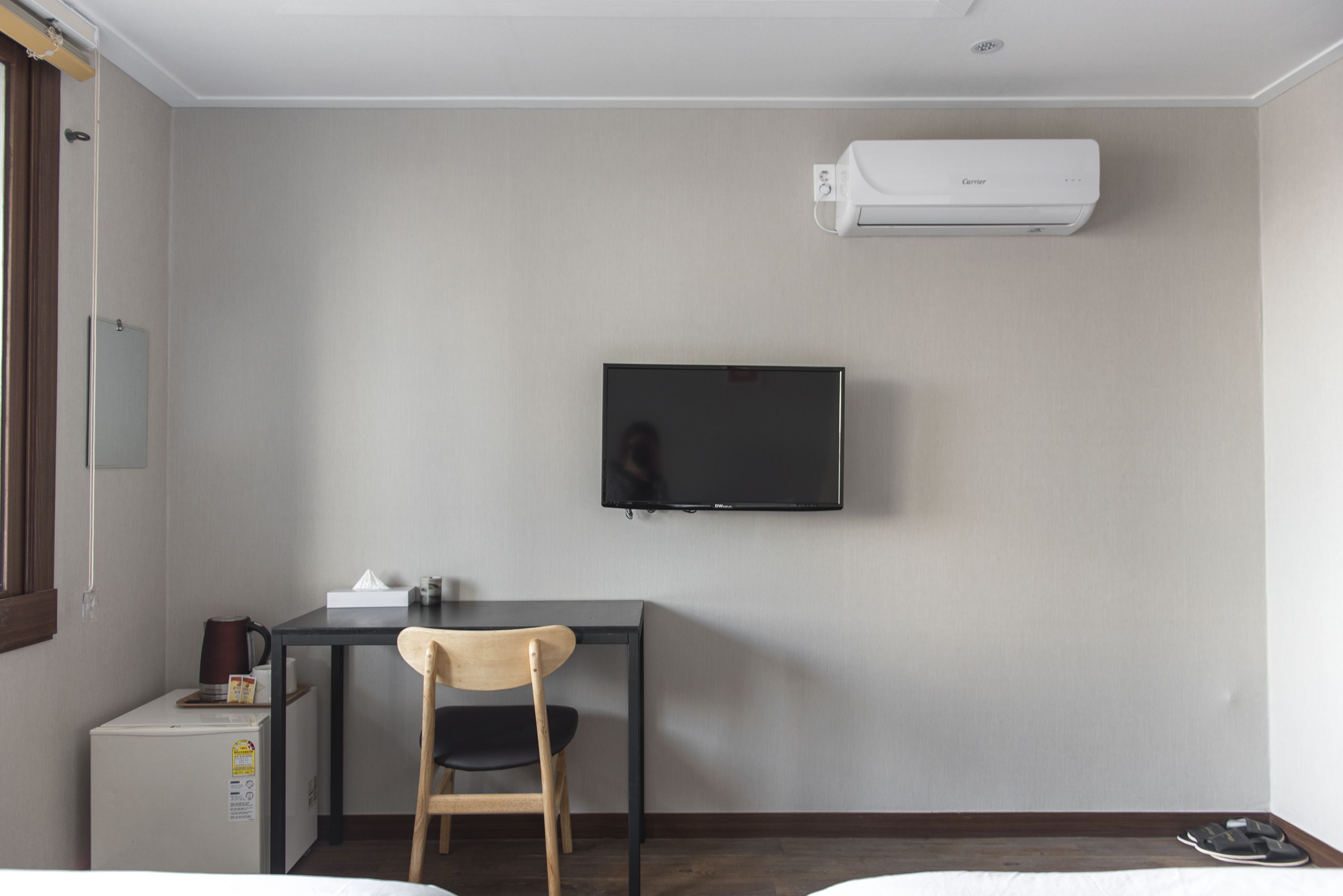 Une chambre d’hôtel équipée d’un téléviseur à écran plat fixé au mur, d’un petit bureau avec une chaise, d’un mini-réfrigérateur et d’un lit.