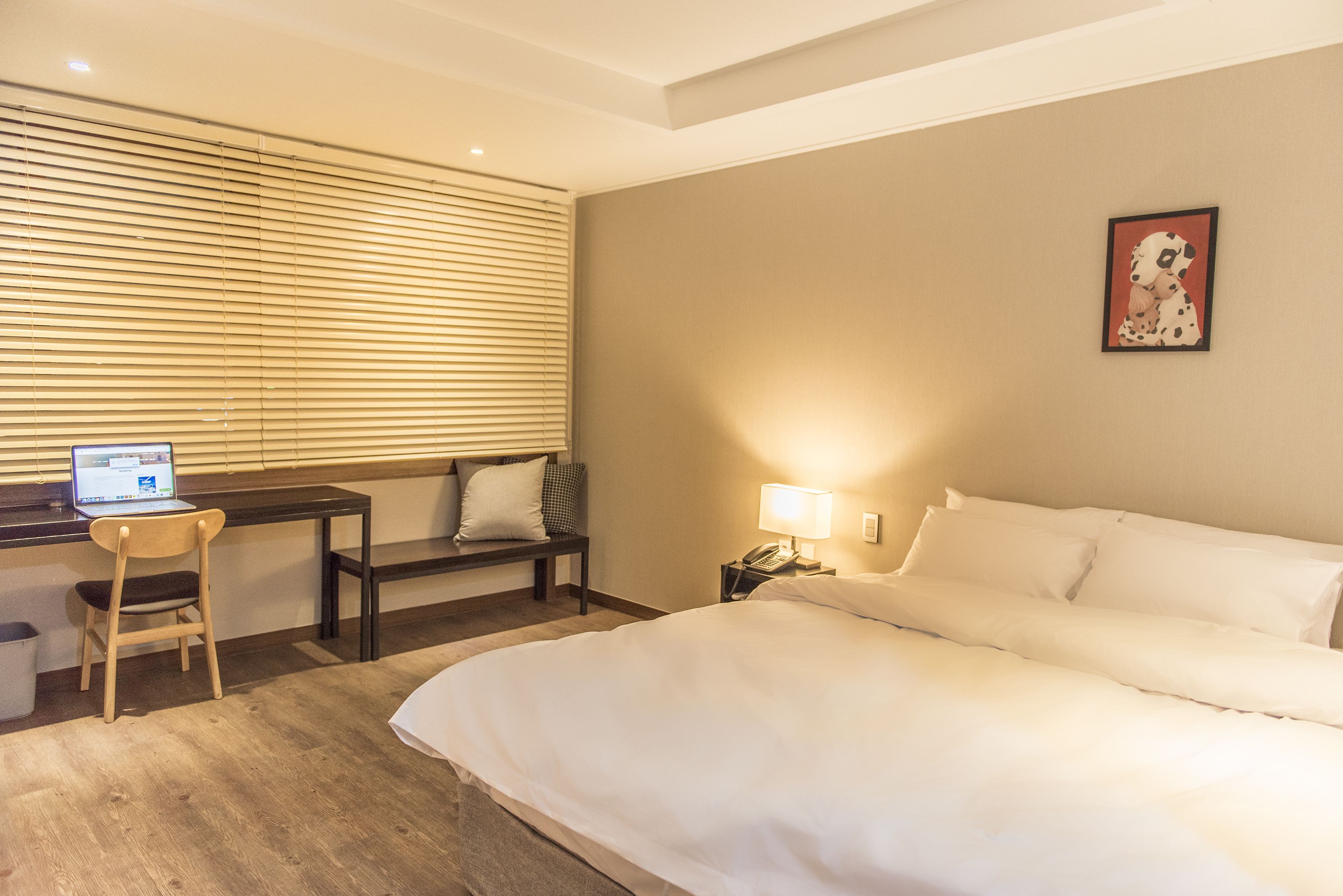 Une chambre d’hôtel avec un lit, un bureau avec un ordinateur portable, une chaise, une lampe et un tableau au mur.
