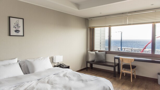 A hotel room with a large bed, a desk, a chair, and a window with a view of the sea. - Check Inn Hotel Jeju (Jeju City)
