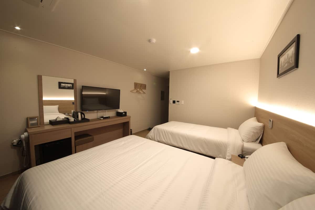 A hotel room with two beds, a TV, a desk with a mirror, and a wall-mounted picture.