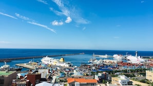 A coastal port with multiple ships docked, a lighthouse, and a variety of buildings including residential and commercial structures. - Harbor Hotel (Jeju City)