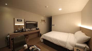 Una habitación de hotel con cama, escritorio con televisor, silla, mesita de noche con teléfono y lámpara de pared.