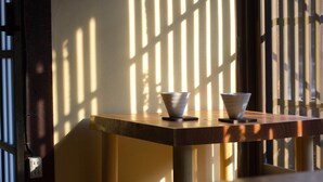 A wooden table with two bowls on it, positioned near a window with vertical blinds casting shadows. - Guesthouse MADO – Hostel (Nagoya)