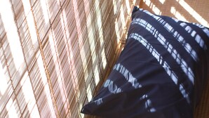A close-up of a patterned pillow against a woven wall, with sunlight casting shadows. - Guesthouse MADO – Hostel (Nagoya)