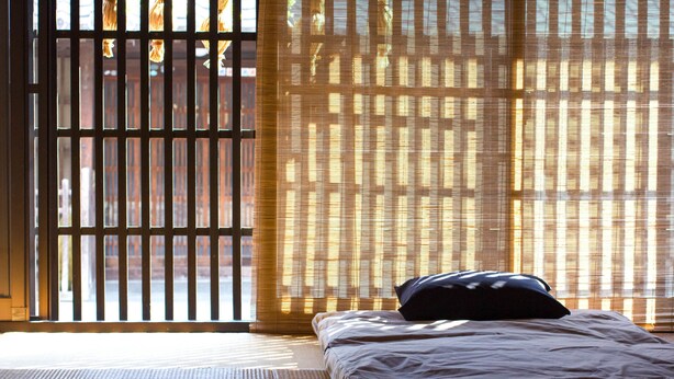 A room with a bed, a window with blinds, and a view of buildings outside. - Guesthouse MADO – Hostel (Nagoya)