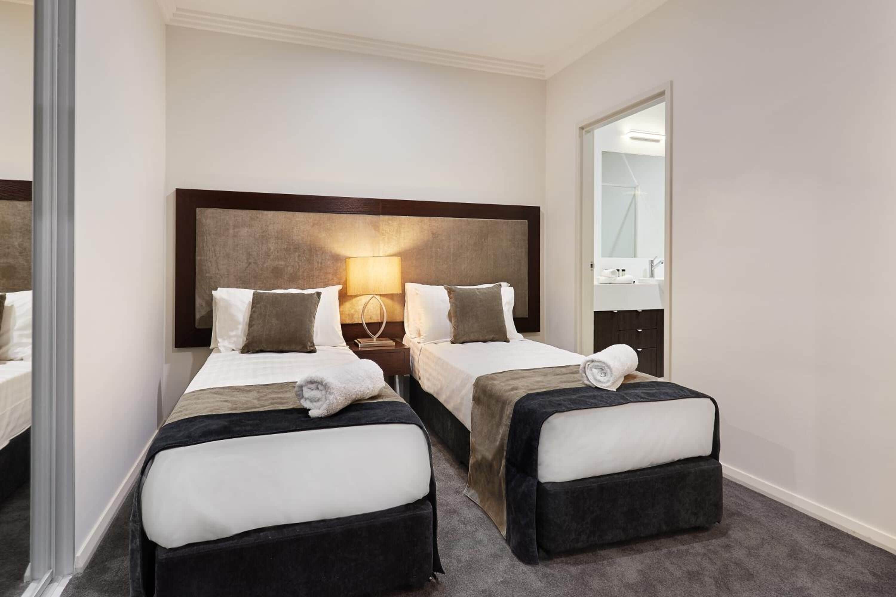 Ein Hotelzimmer mit zwei Betten, einem großen Spiegel und einem durch eine offene Tür einsehbaren Badezimmer.