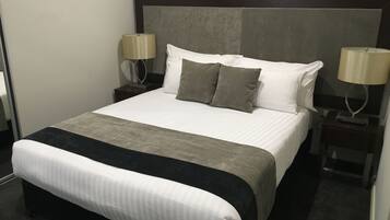 A neatly made bed with a grey and white bedspread, two grey pillows, and two bedside lamps on either side.