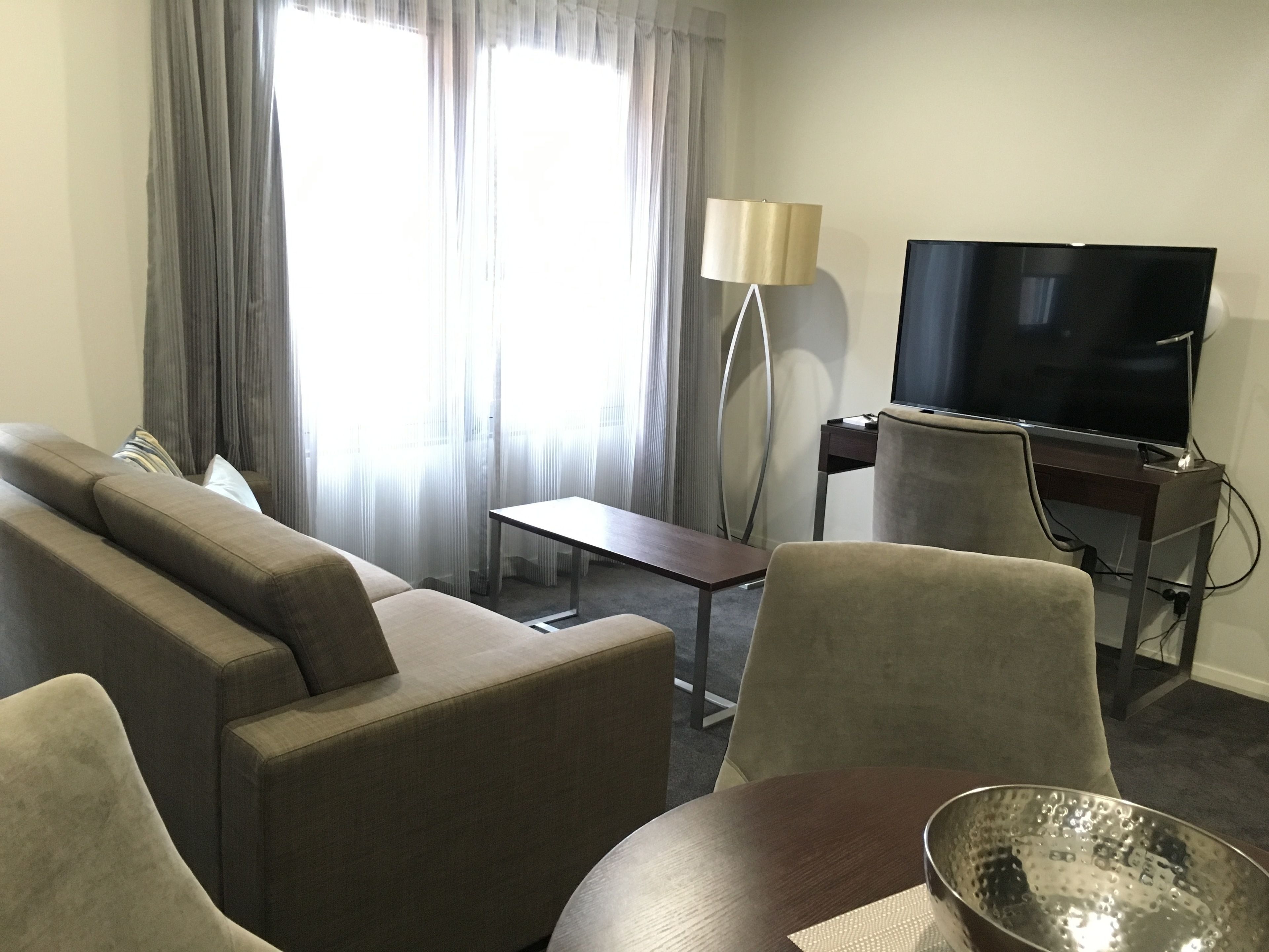 A hotel room with a sofa, armchairs, a small table, a TV, and a lamp.