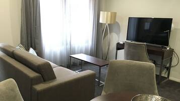 A hotel room with a sofa, armchairs, a small table, a TV, and a lamp.