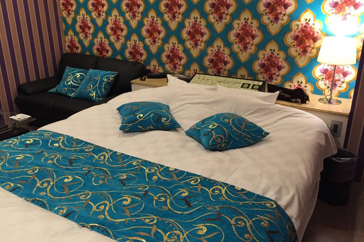 A hotel room with a bed, a nightstand, a lamp, and a wall with a floral pattern.