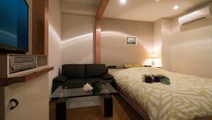 Ein gemütlicher Raum mit Bett, Sofa, Glastisch, Fernseher und Klimaanlage.