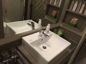 Een badkamer met een witte wastafel, een spiegel en planken met toiletartikelen.