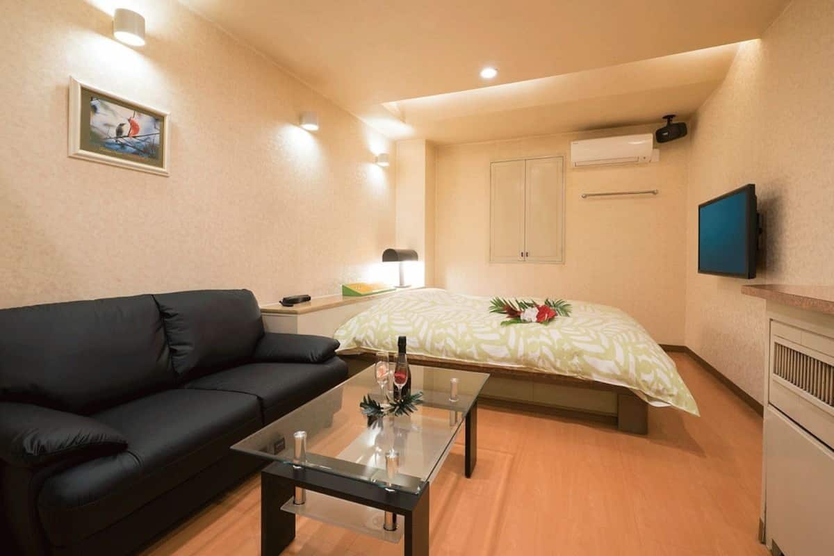 A compact hotel room with a bed, a sofa, a small table, a TV, and a picture on the wall.
