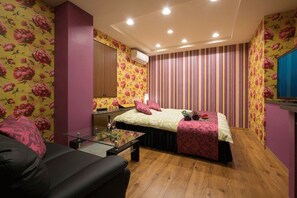 Een slaapkamer met een bed, een glazen salontafel, een zwarte bank en een houten vloer.