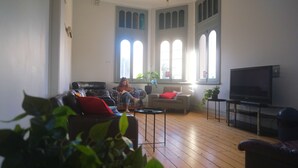 A living room with a leather sofa, a red cushion, a television, and a potted plant. - Britannia on William - Hostel (Perth)