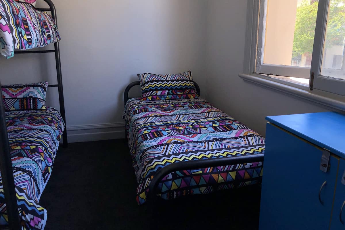Ein Schlafsaalzimmer mit Etagenbett, Einzelbett und einem blauen Schrank.