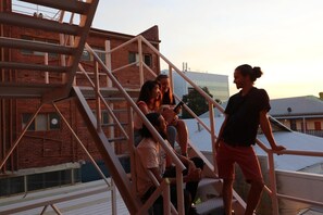 A group of people on a rooftop with a staircase and a brick building in the background. - Britannia on William - Hostel (Perth)