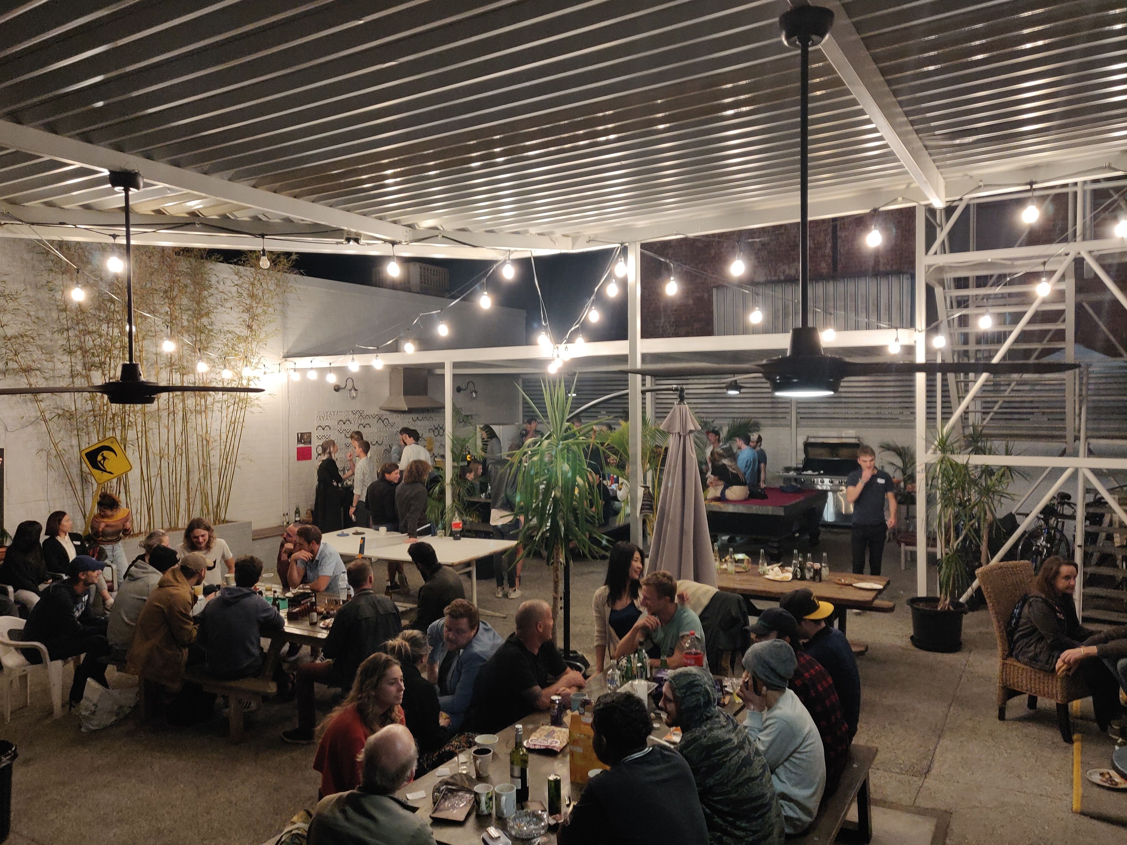 Un comedor interior con mesas y sillas, un escenario con un piano, y una multitud de personas.