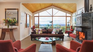 A spacious living room with a large window, a fireplace, and a leather sofa. - Chalet Eiger Lodge (Taupo)