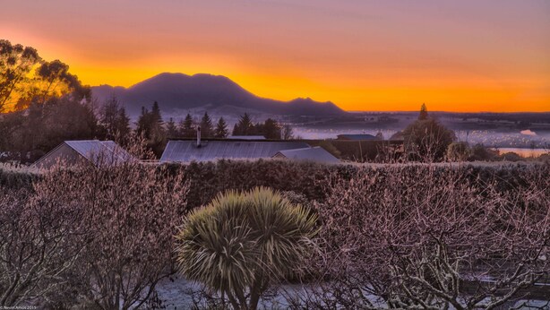 A landscape with a mountain range, a house with a sloped roof, and sparse vegetation. - Chalet Eiger Lodge (Taupo)