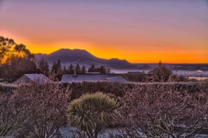A landscape with a mountain range, a house with a sloped roof, and sparse vegetation. - Chalet Eiger Lodge (Taupo)
