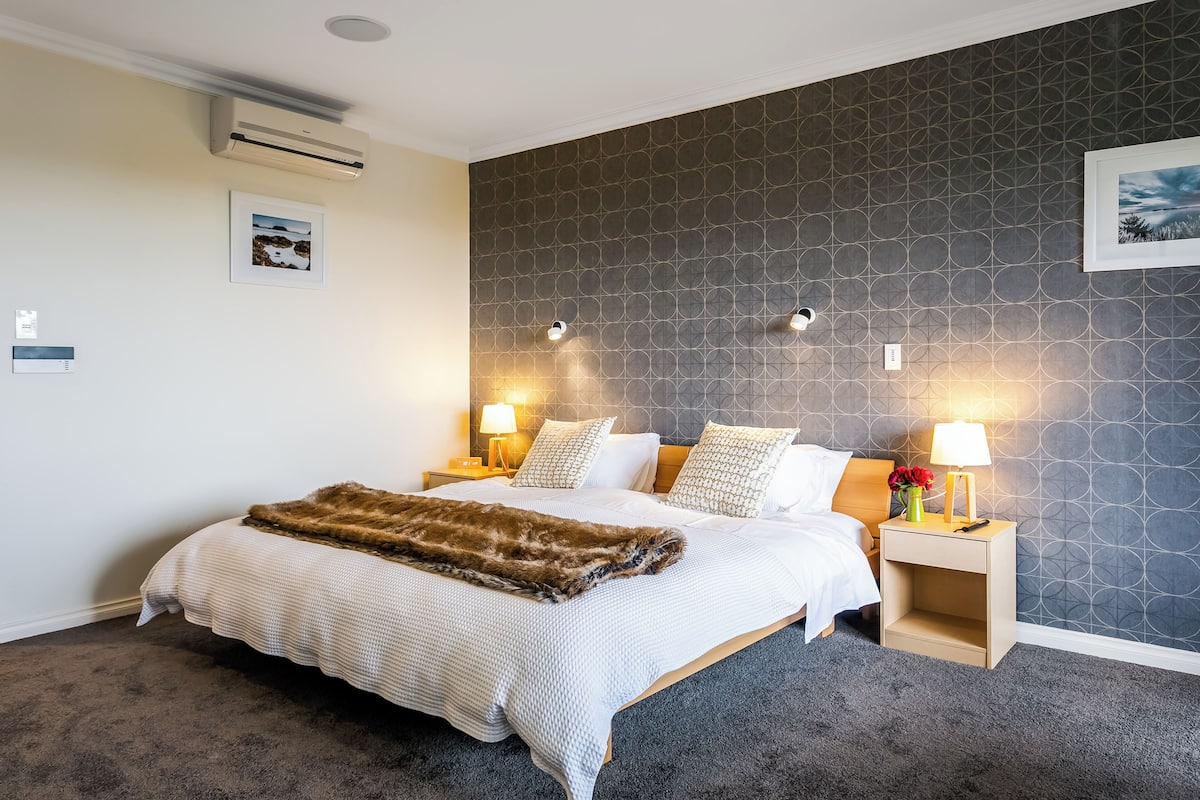 A neatly made bed with a white and brown blanket, two bedside tables with lamps, and a patterned wall.