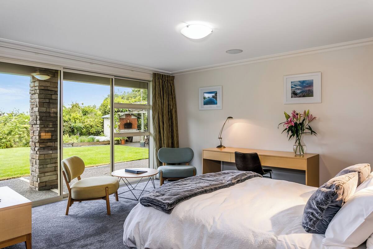 A hotel room with a large bed, a desk, a chair, and a view of the outdoors.