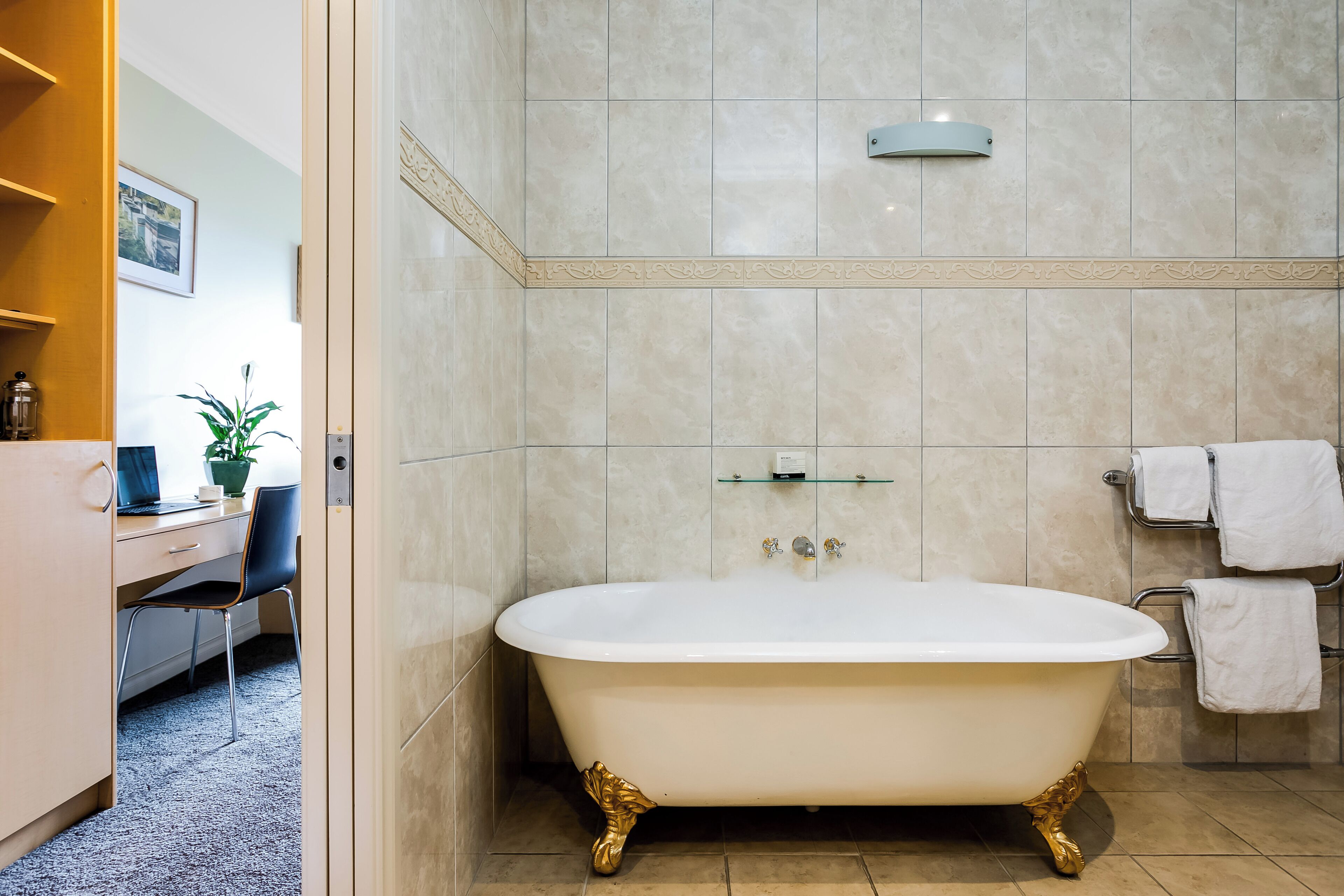 A bathroom with a freestanding bathtub, a towel rack, and a shelf with a glass top.
