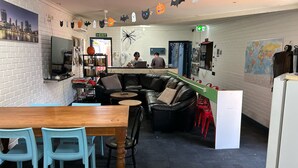 A cozy cafe with a brick wall, a black leather couch, a wooden table, and blue chairs.