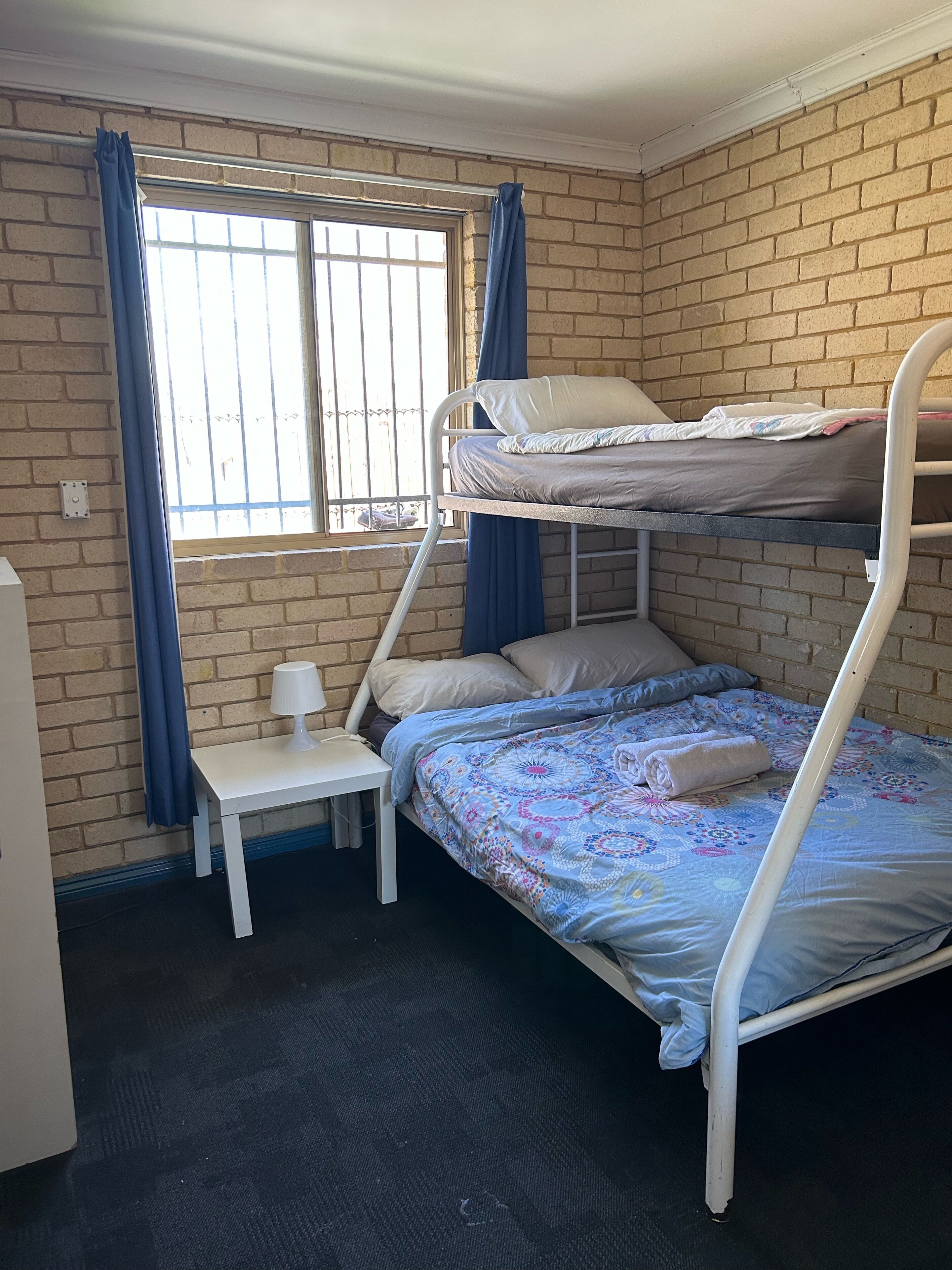 A bunk bed room with a window, a small table with a lamp, and a brick wall.