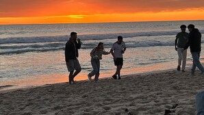 A beach scene with people walking along the shore during sunset.