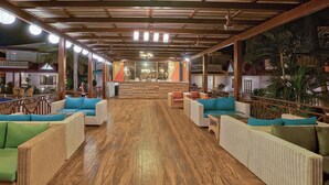 A spacious lobby with wicker furniture, wooden flooring, and a view of the pool area.
