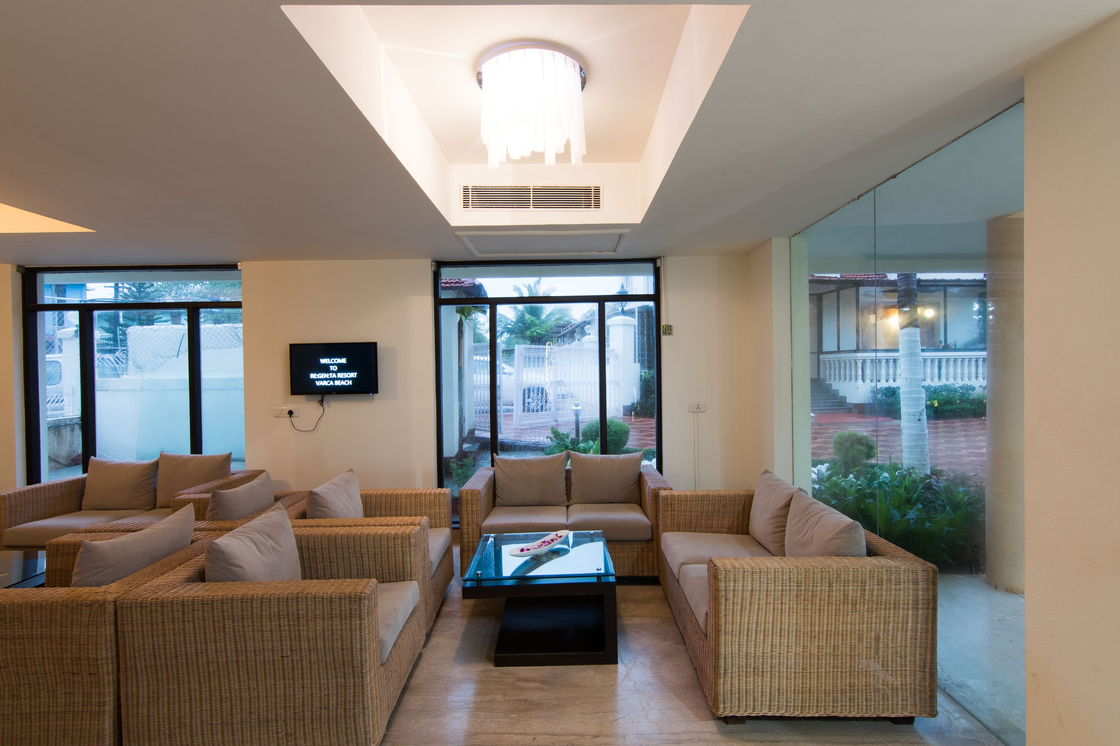 A spacious living area with wicker furniture, a flat-screen TV, and large windows offering a view of the outdoors.