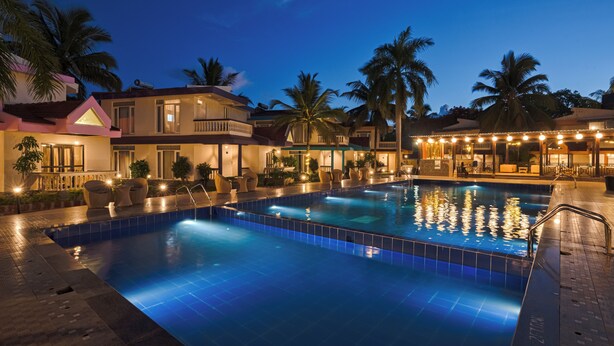 A swimming pool with a tiled deck, surrounded by palm trees and a building with multiple balconies.