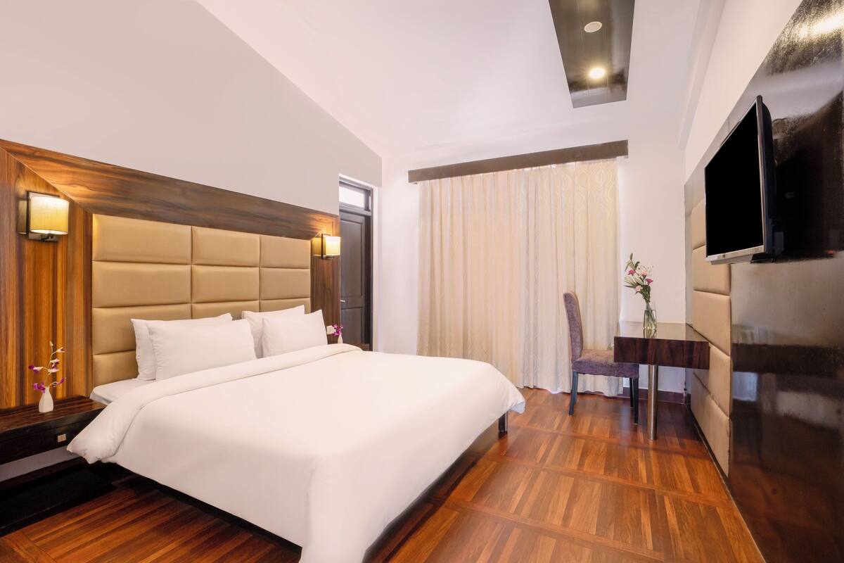 A modern hotel room with a large bed, wooden flooring, a flat-screen TV, and a seating area with a chair and table.