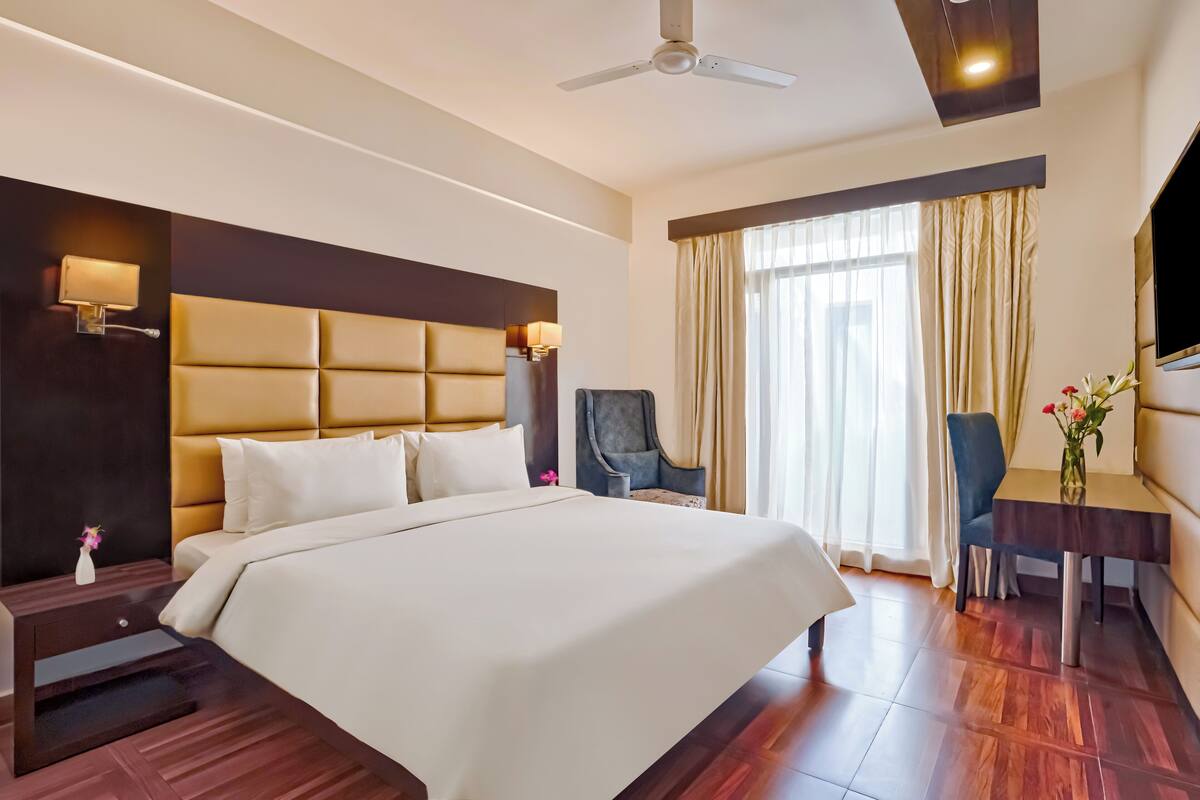 A hotel room with a large bed, a desk, a chair, a TV, and a ceiling fan.