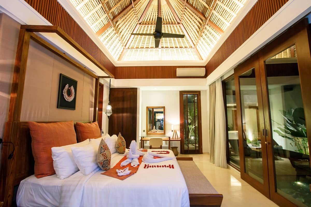 A hotel room with a large bed, a desk, a mirror, and a sliding glass door leading to a balcony.