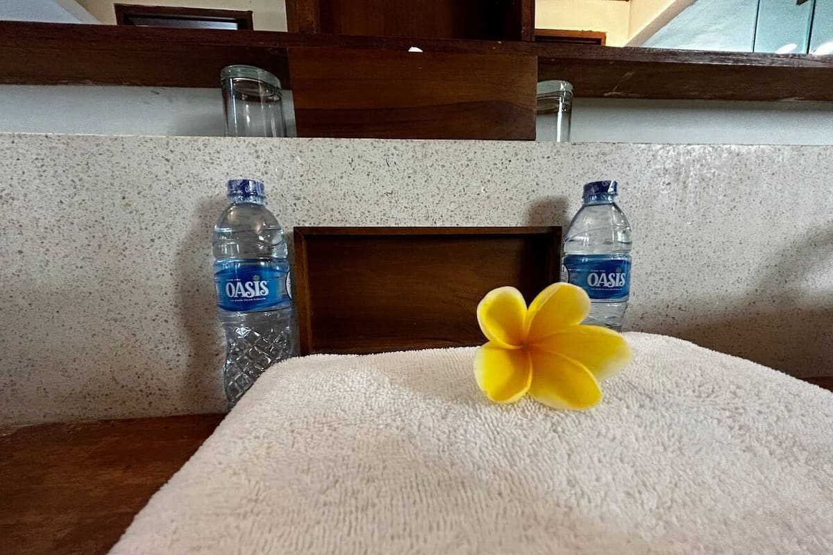 A bathroom with a wooden headboard, two bottles of Oasis water, and a yellow flower on a white towel.